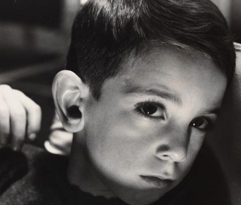 Photo portrait of a young white boy. His head is turned down but he looks up at the camera. A shadow crosses his face.