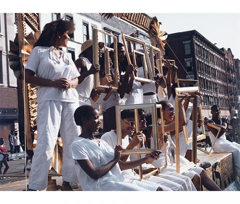 African-American people dressed in white sit on a float holding gold picture frames