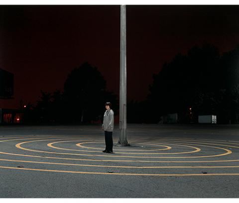 night, boy standing near a pole in the center of a series of yellow concentric circles