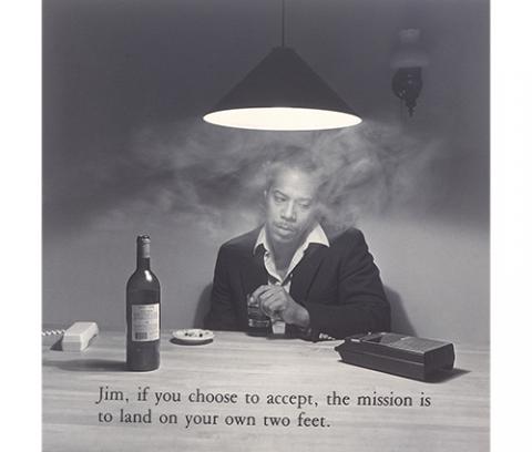 African American man seated at a table with a lamp hanging overhead; holding a glass with left hand; tape recorder on table at left; telephone on table at right; smoke surrounding portrait; text at the bottom reads, "Jim, if you choose to accept, the mission is to land on your own two feet."