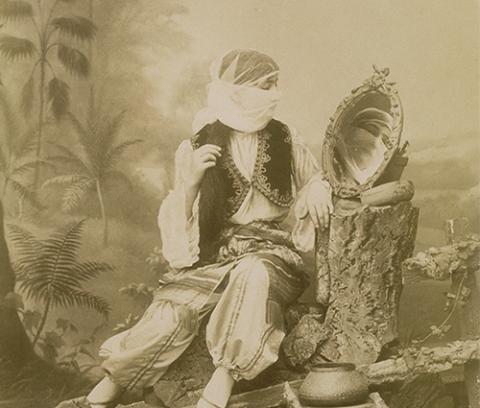 Seated woman with veil looking into a mirror, trees in the background