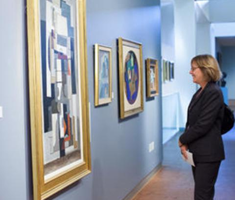 profile view of a woman in an art gallery, looking at paintings on a wall