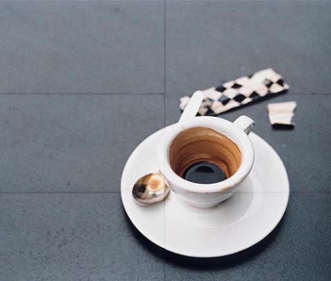 grey table top with white used coffee cup and saucer, used spoon and open black and white checked sugar packet