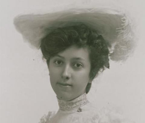 close-up of woman with fancy updo in her hair, wearing a white hat and a white dress with a high collar