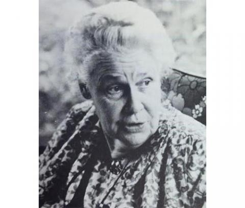 older woman with hair tied up, wearing a floral top, looking to her left