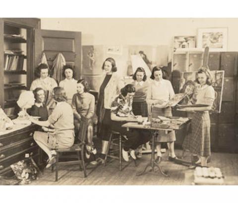 a group of women in an art studio. some sitting, drawing or talking with one another. others stand and observe the work being done.