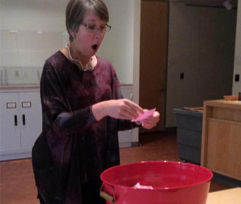 woman pulls a slip of paper out of a red bucket with surprised expression in her face