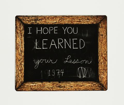 Image of small student chalkboard in wooden frame on a white background with a message in straighthand and cursive writing: "I HOPE YOU LEARNED your lesson / 1974 W," with faint barely visible errors crossed out and erased behind
