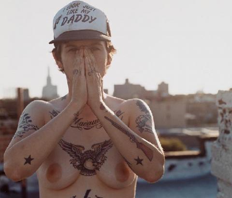 exterior, city rooftops, young woman, nude from waist up, with numerous tattoos on her body, both hands over her face, wearing baseball cap with "I look just like my daddy" on it