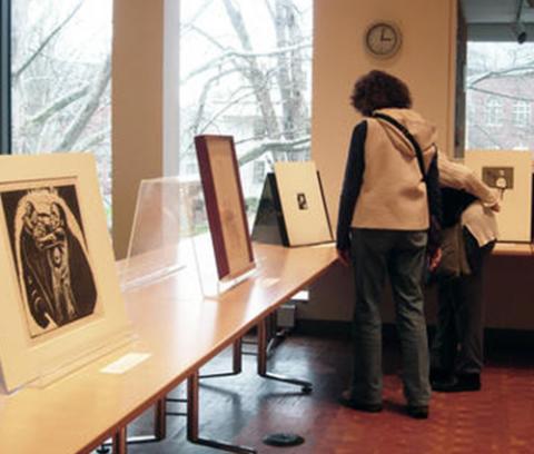 white table with prints propped up on it; two women stand in the corning looking at the prints