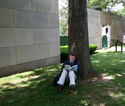 man sitting on grass under a tree, reading a book