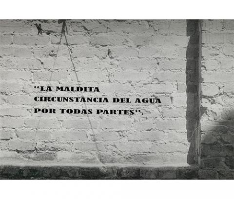 brick wall with indentation and applied text: 'LA MALDITA / CIRCUNSTANCIA DEL AGUA / POR TODAS PARTES".