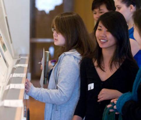 group of students stands looking at a display of prints propped up on a tabletop