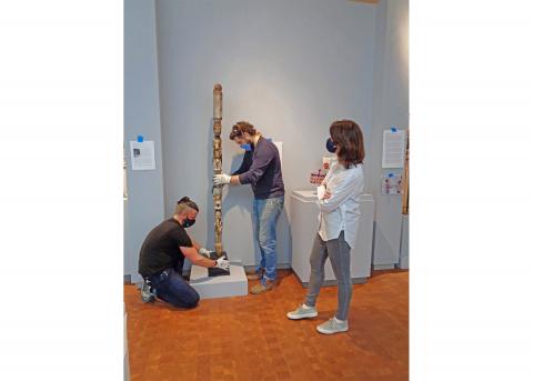 two preparators install artwork as another museum professional watches