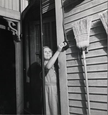 girl reaching through a screen door to turn on a light on the right