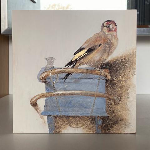 goldfinch sitting atop a pastel blue house on white background