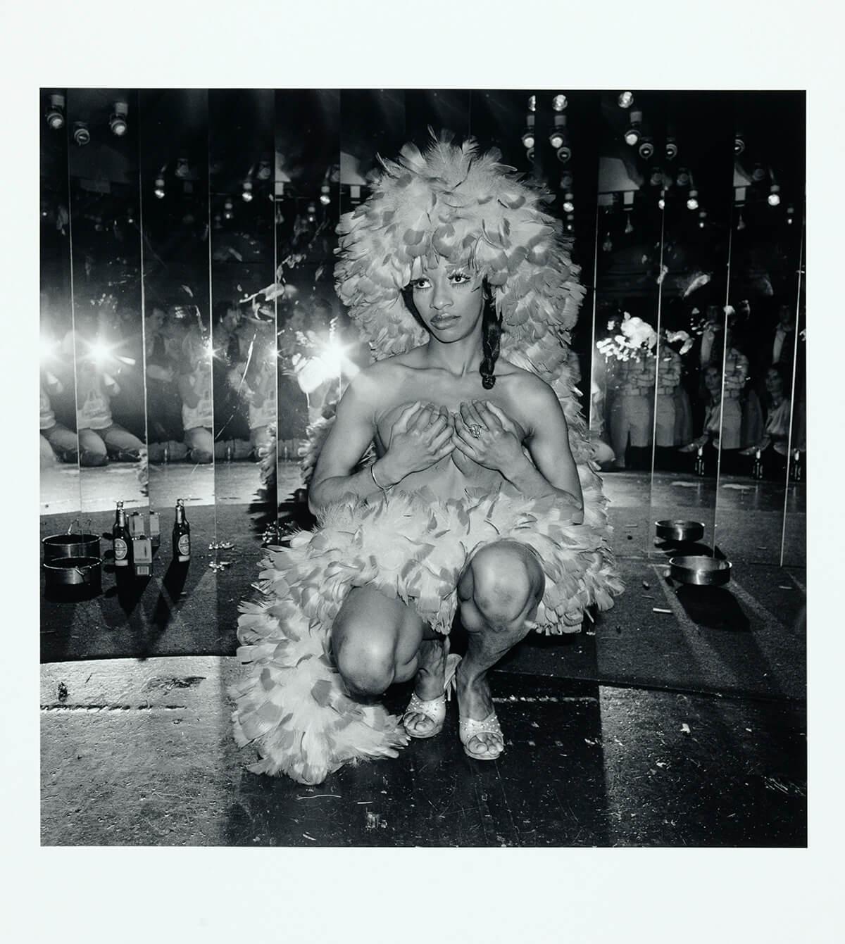 Women with a boa in hair and surrounding body, crouched down in front of mirrors