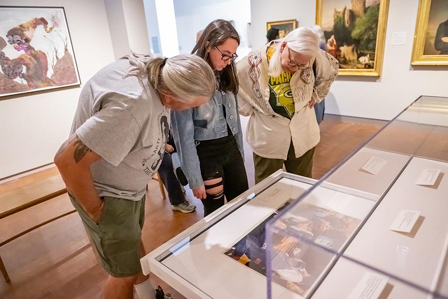 Three people looking at a drawer of works on paper within a gallery