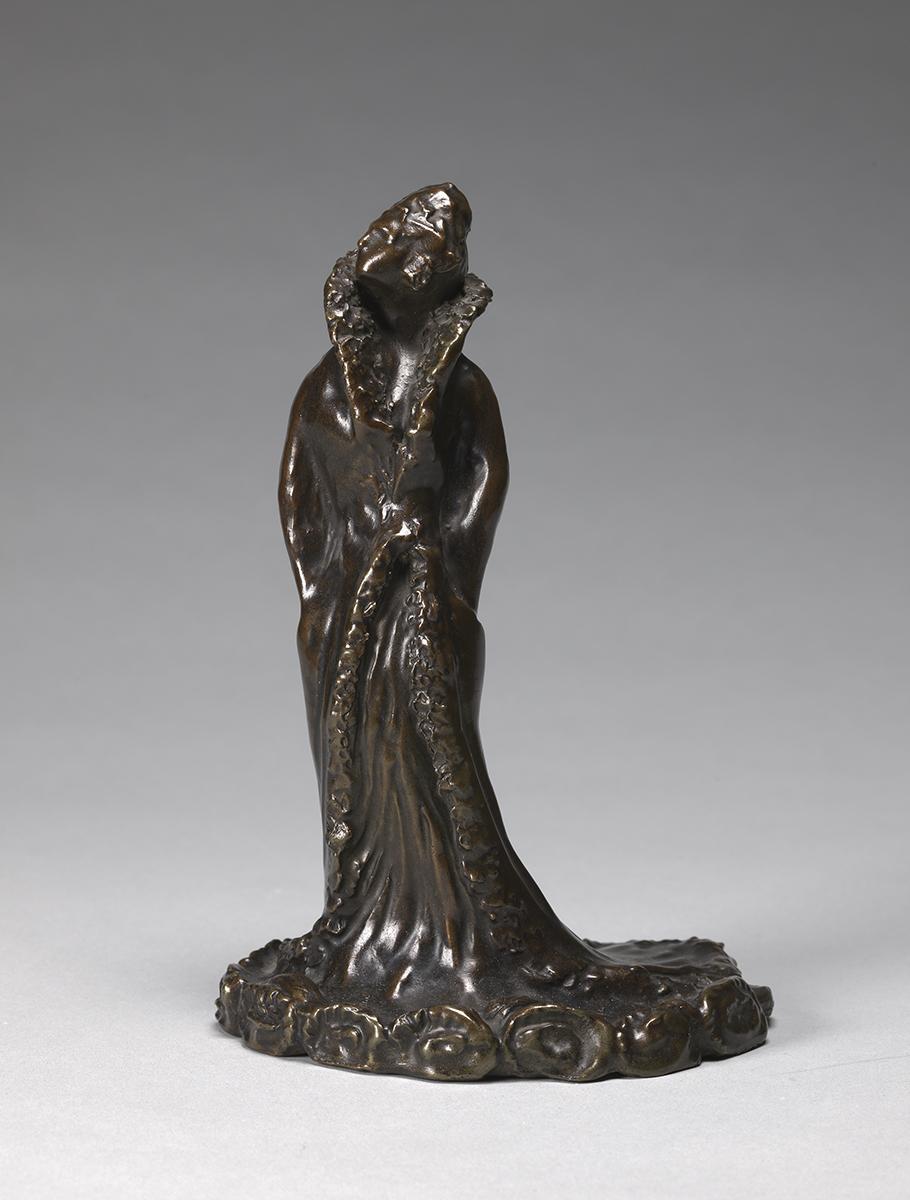 Dark metal sculpture of a woman with hands in pockets wearing a flowing gown that covers the floor around her feet