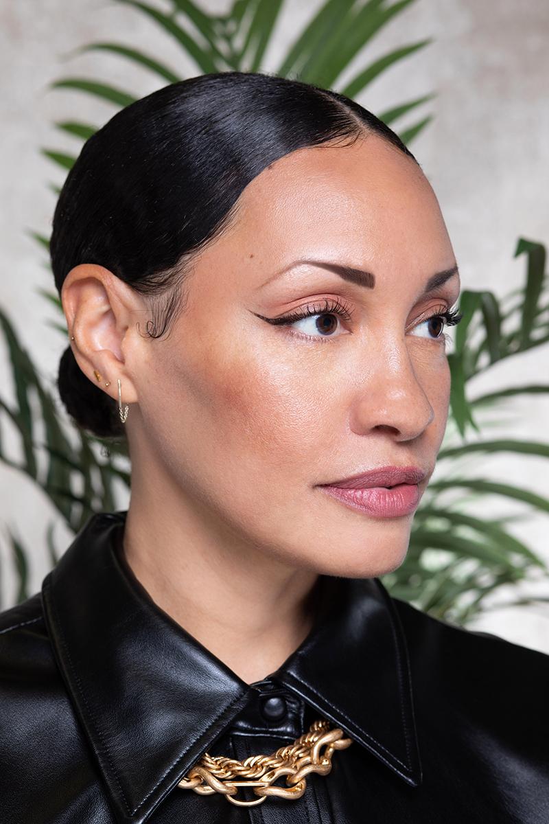 Portrait photo of a person with black dress, gold necklace and hair pulled back tightly