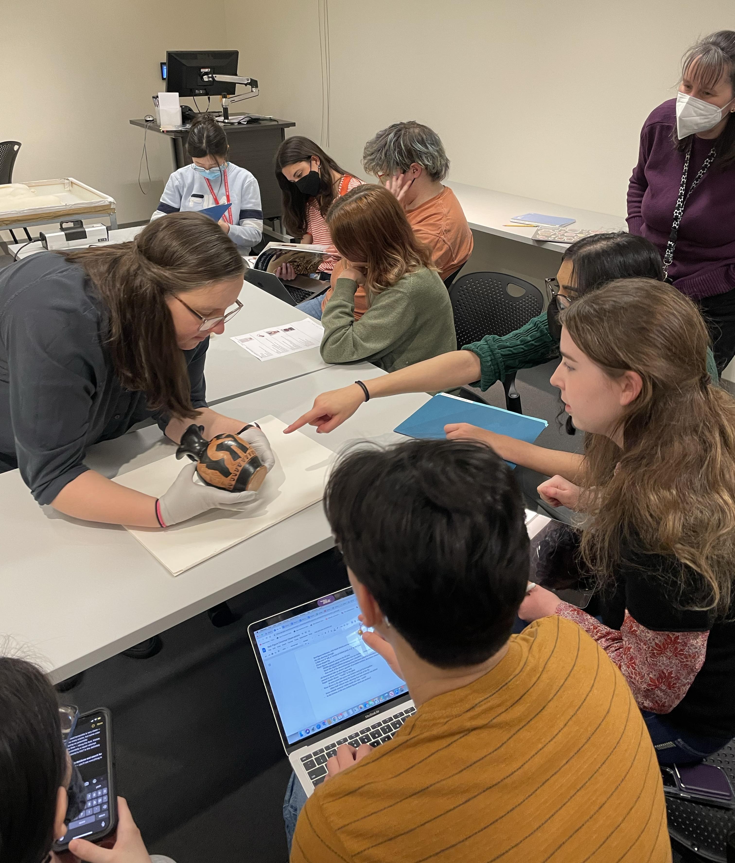 Students working with museum expert who is holding a Greek vase