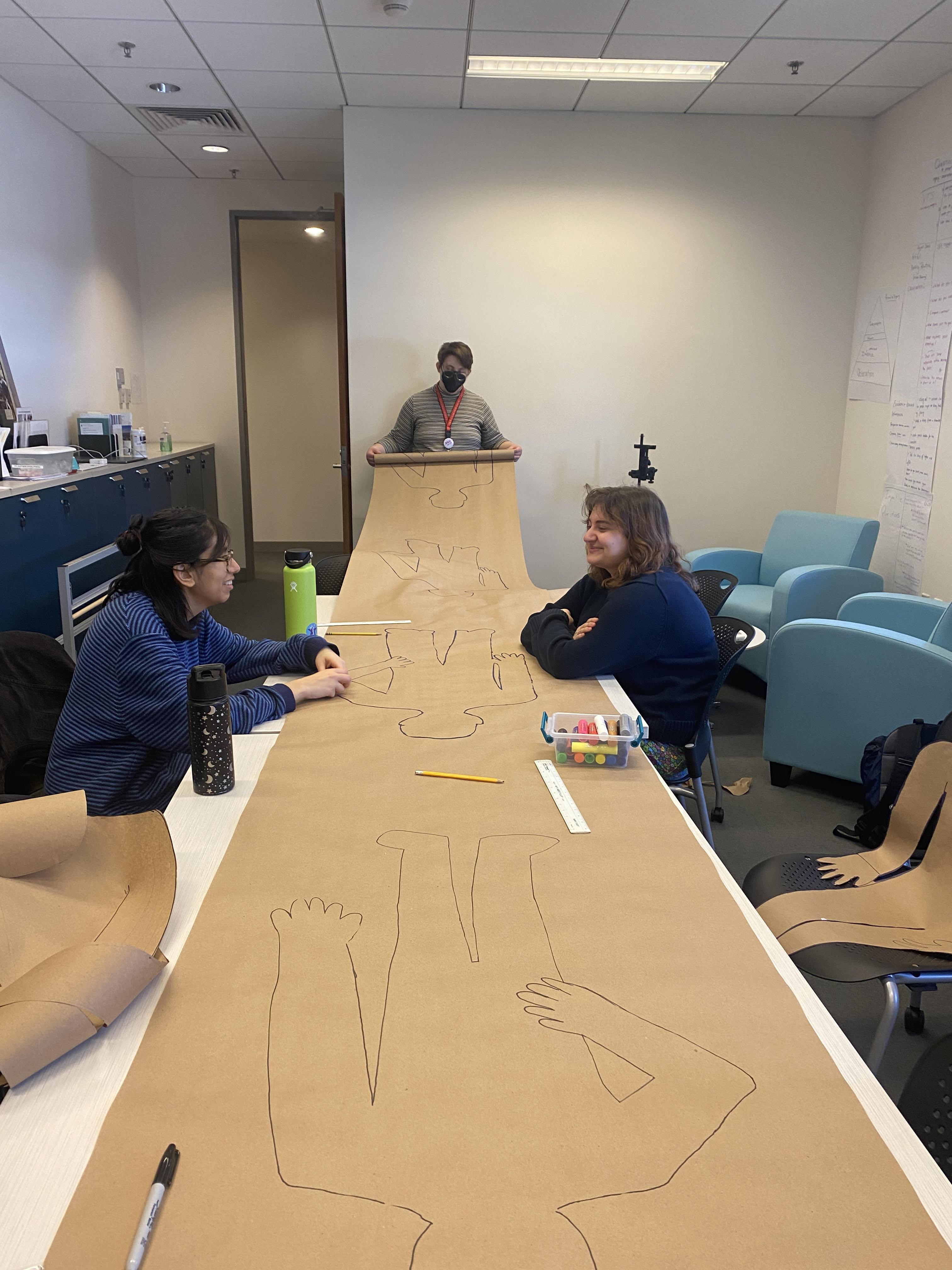 Three students drawing on a long sheet of craft paper for an event