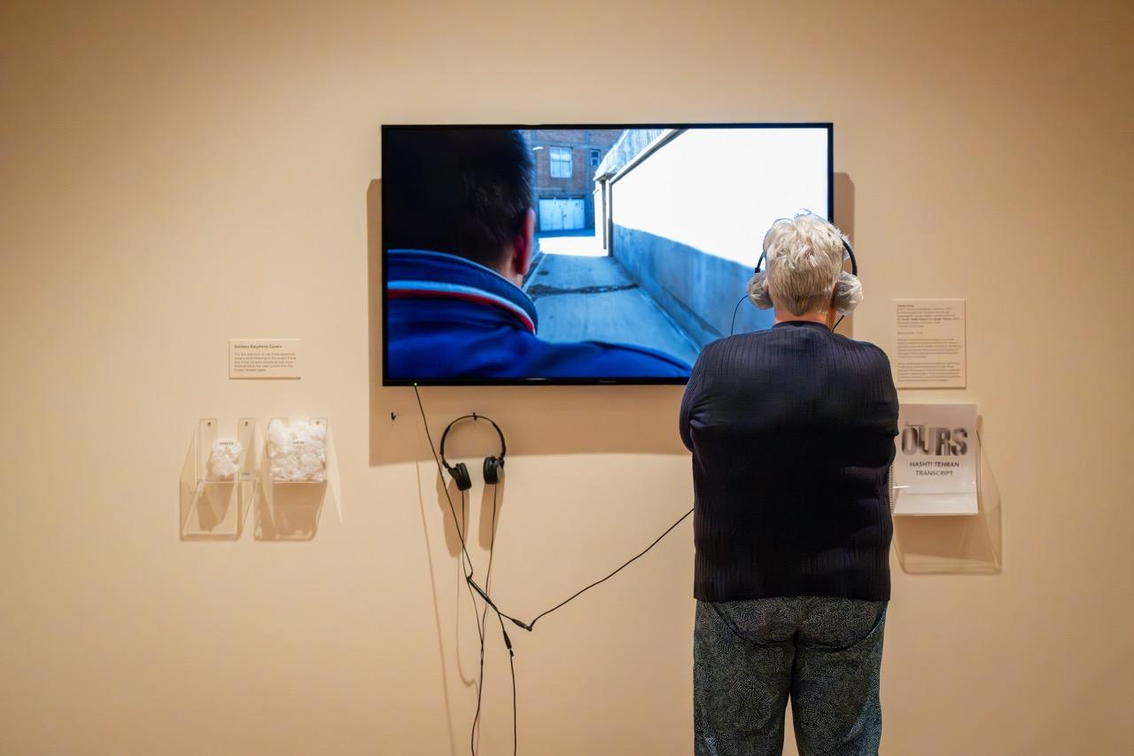 A person with headphones on listening t and watching a video being played on a wall-mounted monitor