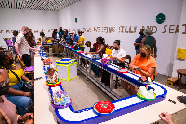 People sit around a conveyor belt interacting with art as it moves around.