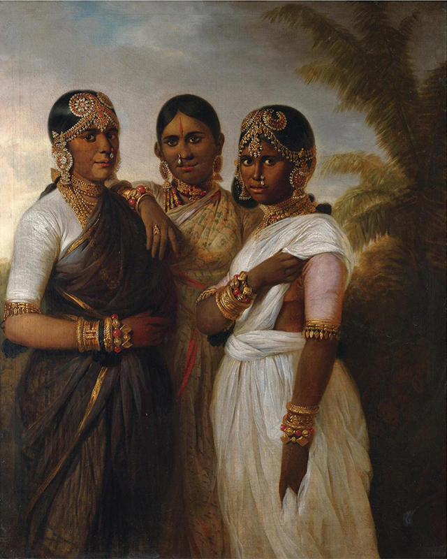 "three women standing wearing saris and ornamental jewelry; woman on the right is showing a bandage on her bicep"