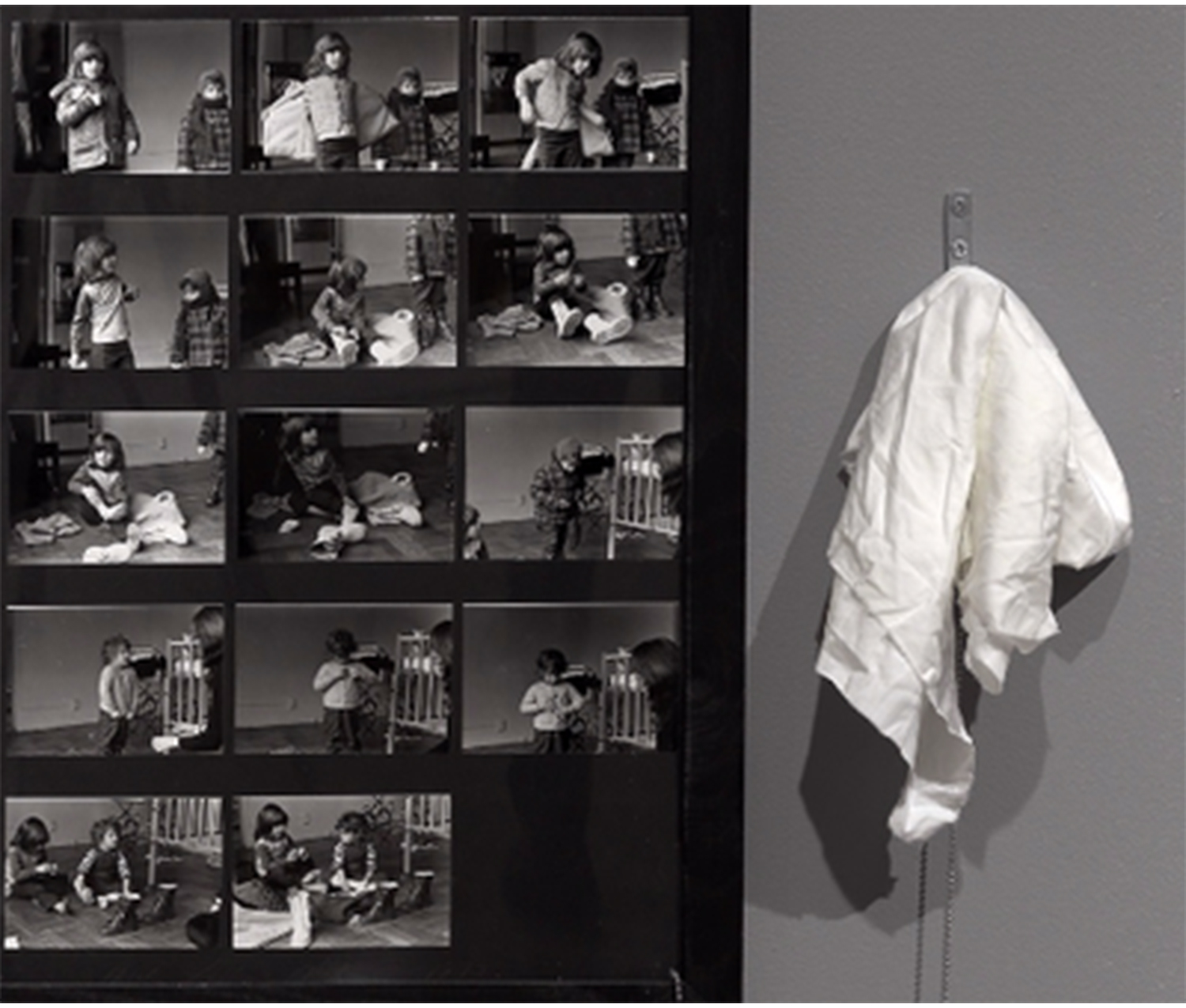 on the left, the edge of an artwork containing black and white images of children getting dressed; on the right, a white rag hanging from a chain