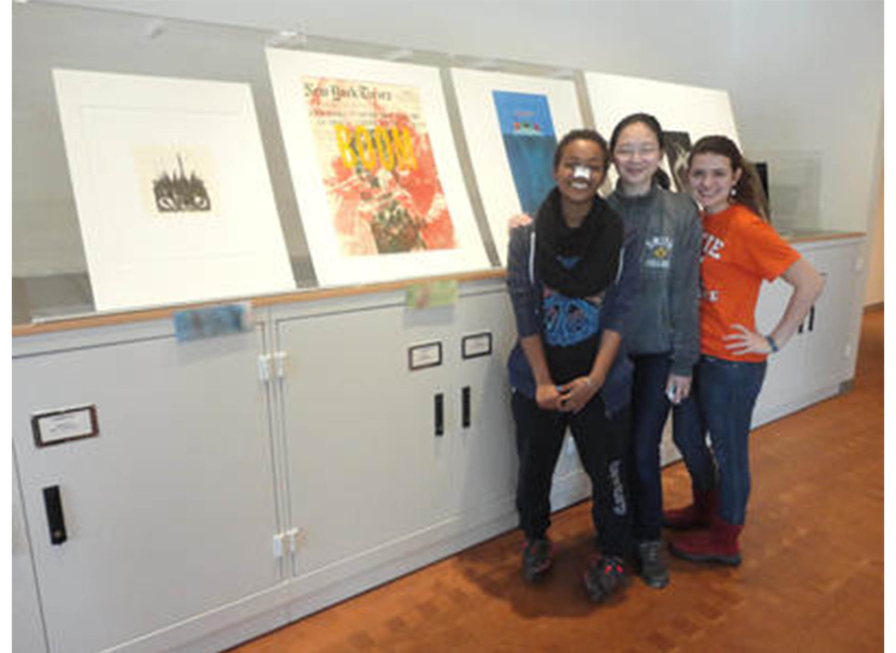 three students standing in front of a display of prints and smiling